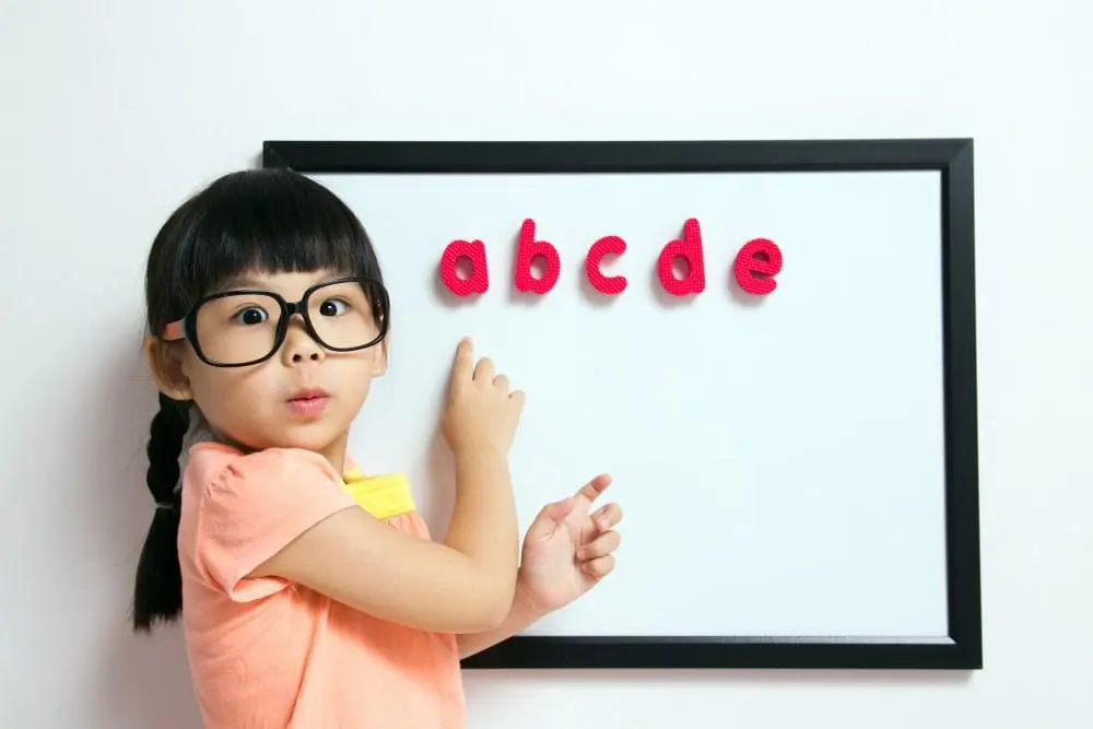 a little girl with glasses points to a board with letter magnets on it