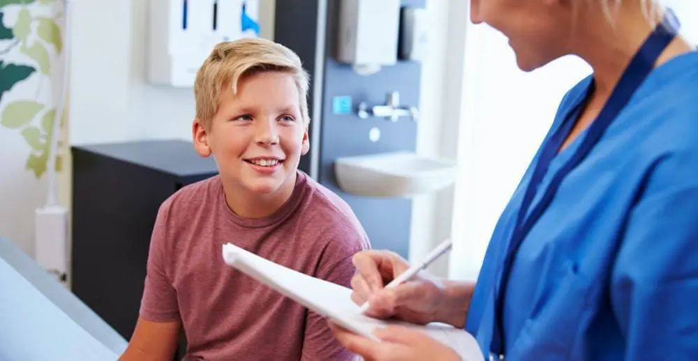 a nurse it writing on a piece of paper while talking to an older young boy