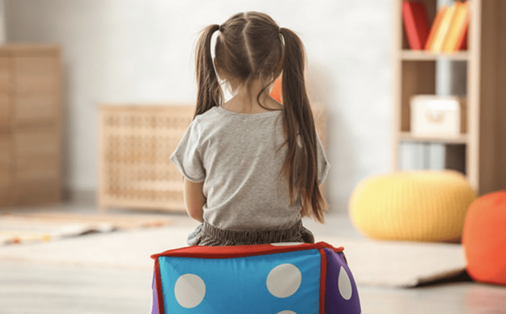 a young girl sits on a dice bean bag facing away from the camera
