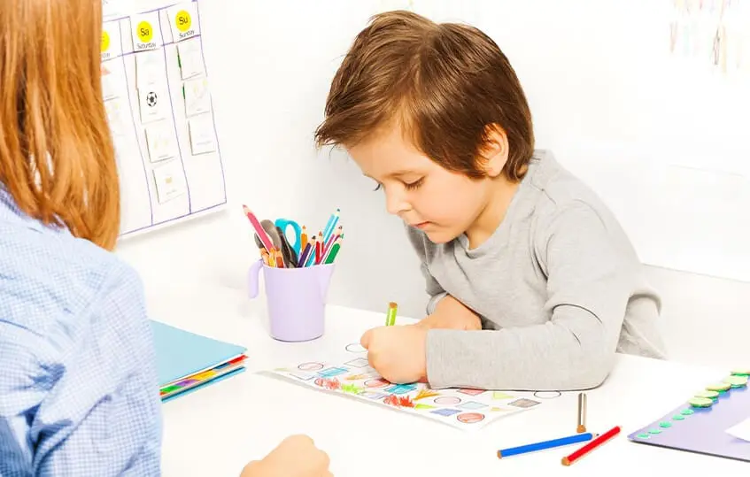a young boy colors while an older woman watches him work