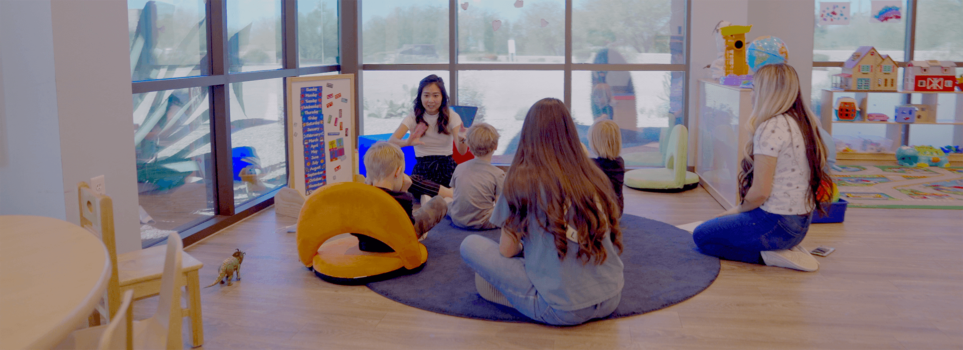 a teacher is surrounded by children engaged in teaching activity with two teachers in the back