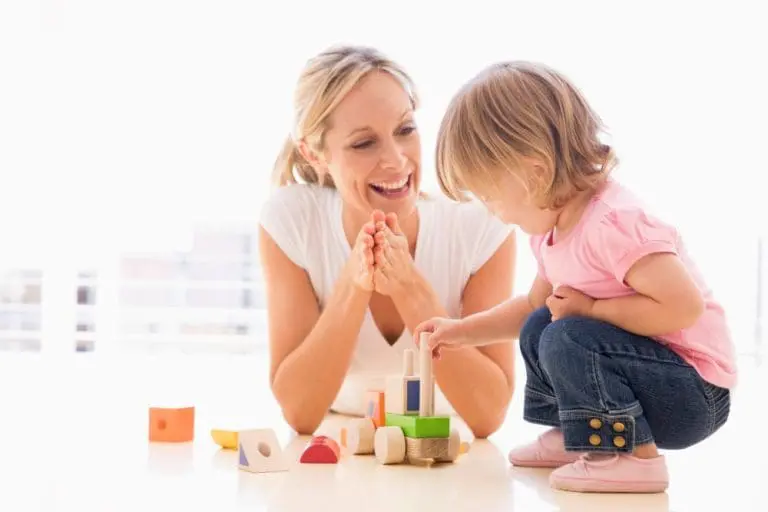 A mom playing with her child as her child builds with blocks.