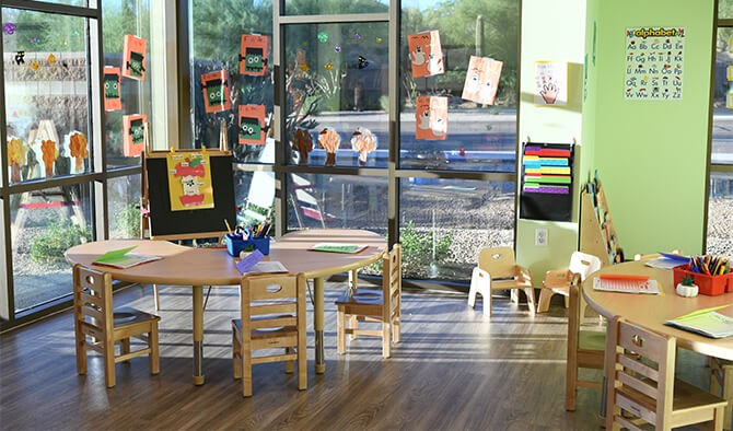 interior of classroom setting with tables, chairs, and art on the windows