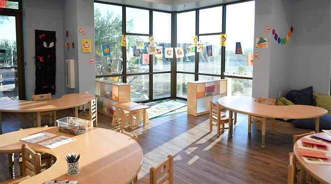 interior of classroom setting with tables, chairs, and art on the windows